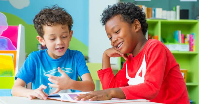 two smiling children looking at a book in a classroom setting