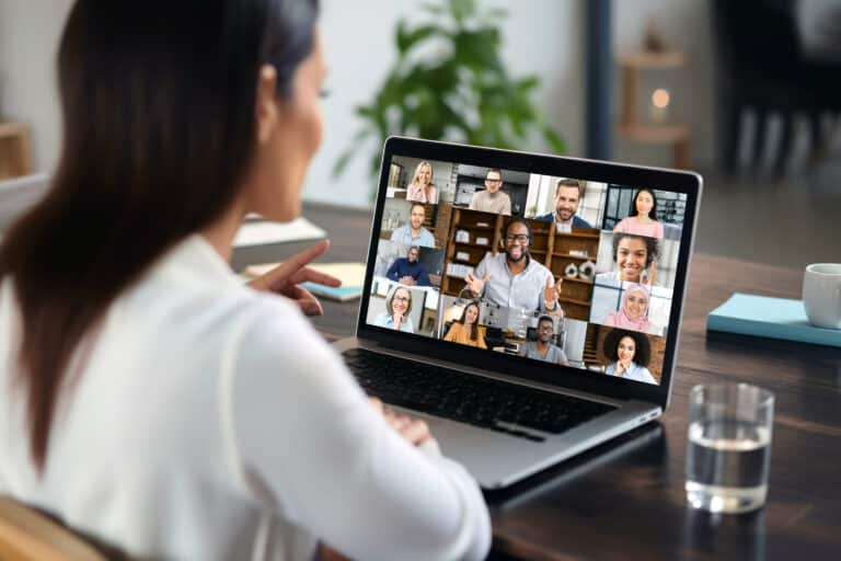 Woman sitting at a desk engaged in a video meeting with several other people.