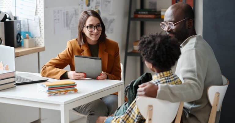 Young teacher having meeting with student and parent, sitting at table and talking together after lessons