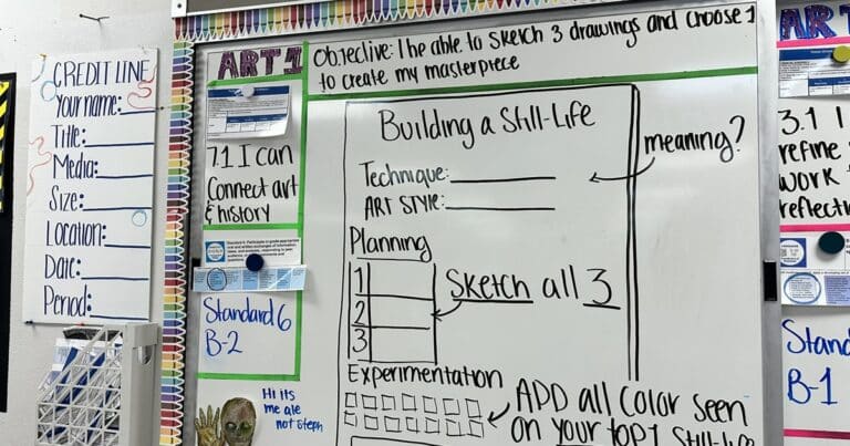 A dry erase board shows an objective for an art class, connecting to standards